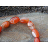 Handmade, natural red-orange agate bracelet, beautiful red nuances 12 mm bead stretch bracelet, close up,  sitting on a rock on the Irish shore in West Cork